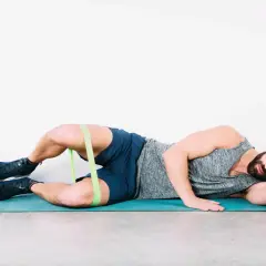 Uomo a terra con elastico intorno alle cosce per esercizi di bandelletta ileotibiale, soluzioni per rafforzare i glutei.
