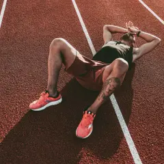 Atleta esausto sdraiato su una pista da corsa, mani sulla testa, forse uno dei sintomi del sovrallenamento.
