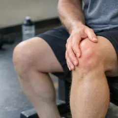 Uomo con mano sul ginocchio, forse un dolore ai tendini della gamba dopo l'allenamento.