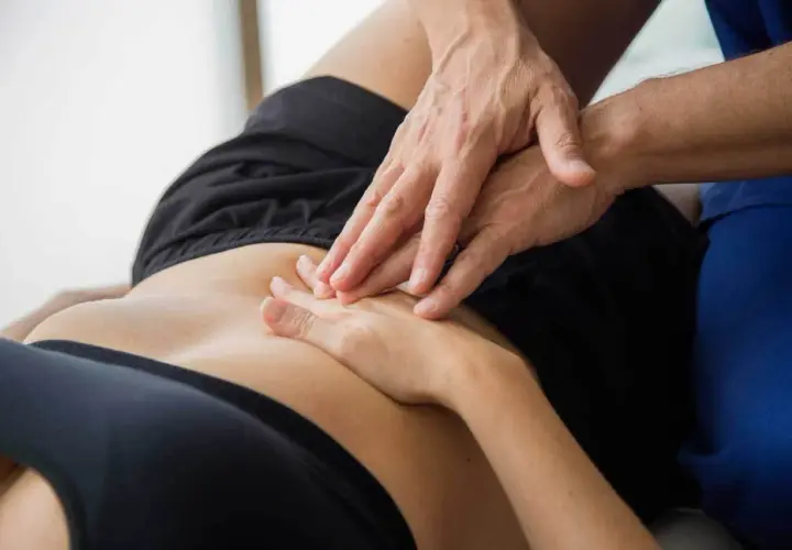 Mani di un fisioterapista che massaggiano l'addome di una persona, aiutando a trattare la pubalgia, un disturbo che può rendere difficili anche i rapporti sessuali.