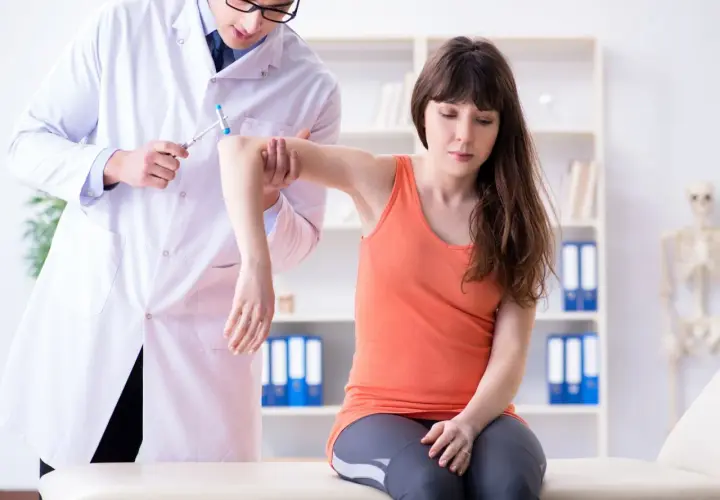 Medico esegue un esame neurologico su una paziente, testando i riflessi del braccio con un martelletto.