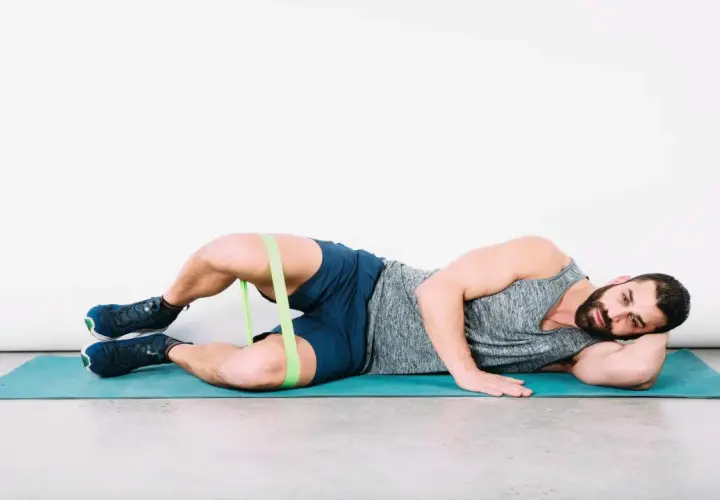 Uomo a terra con elastico intorno alle cosce per esercizi di bandelletta ileotibiale, soluzioni per rafforzare i glutei.
