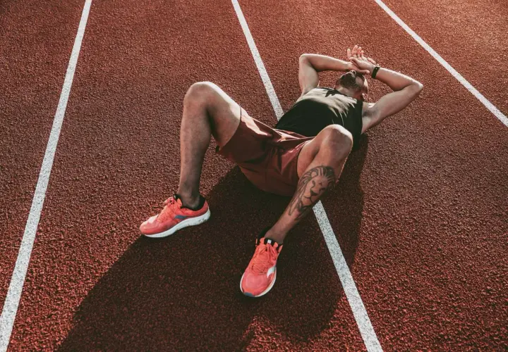 Atleta esausto sdraiato su una pista da corsa, mani sulla testa, forse uno dei sintomi del sovrallenamento.