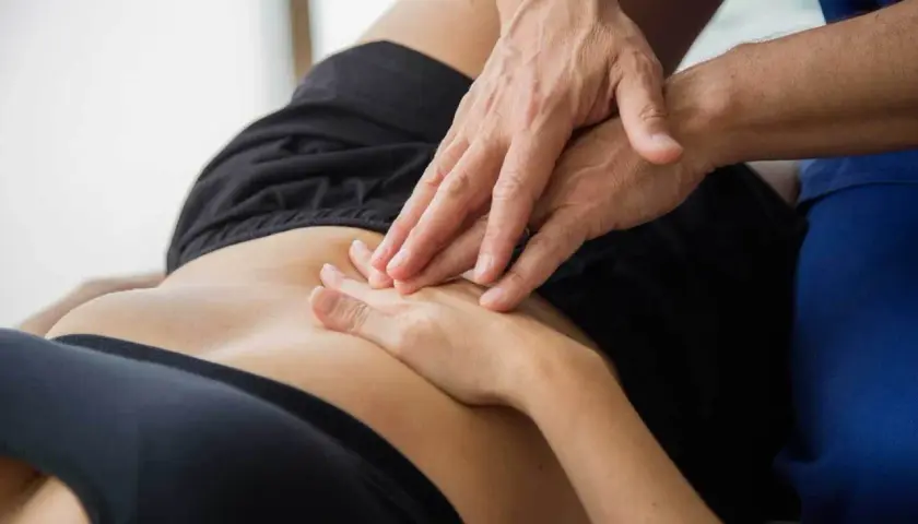 Mani di un fisioterapista che massaggiano l'addome di una persona, aiutando a trattare la pubalgia, un disturbo che può rendere difficili anche i rapporti sessuali.