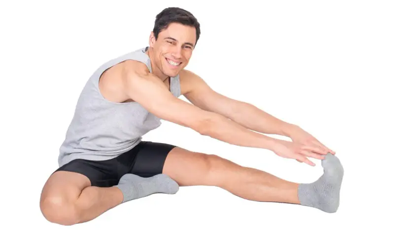 Uomo sorridente fa stretching, allungando la gamba destra. Attenzione a non forzare per evitare una lesione bicipite femorale.