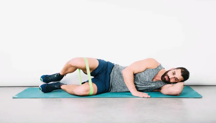 Uomo a terra con elastico intorno alle cosce per esercizi di bandelletta ileotibiale, soluzioni per rafforzare i glutei.