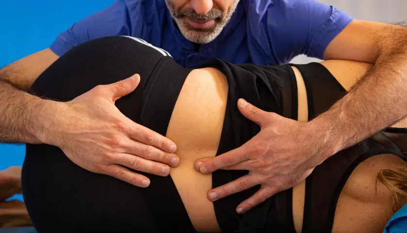 Fisioterapista esamina la schiena di una paziente, valutando la zona lombare per possibili problemi come la stenosi lombare.