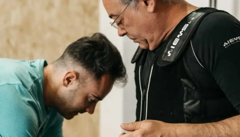 Uomo con giubbotto EMS, assistito da un trainer, per contrastare l'atrofia muscolare.