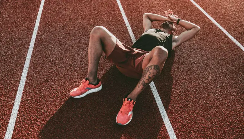 Atleta esausto sdraiato su una pista da corsa, mani sulla testa, forse uno dei sintomi del sovrallenamento.