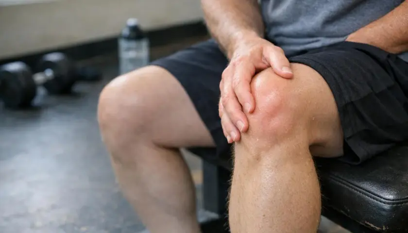 Uomo con mano sul ginocchio, forse un dolore ai tendini della gamba dopo l'allenamento.