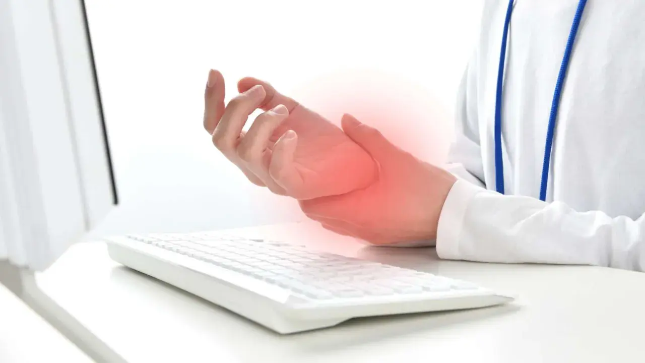 Mano che tiene il polso, con un'area rossa che indica dolore, vicino a una tastiera. Possibili tendiniti diffuse dovute all'uso prolungato del computer.