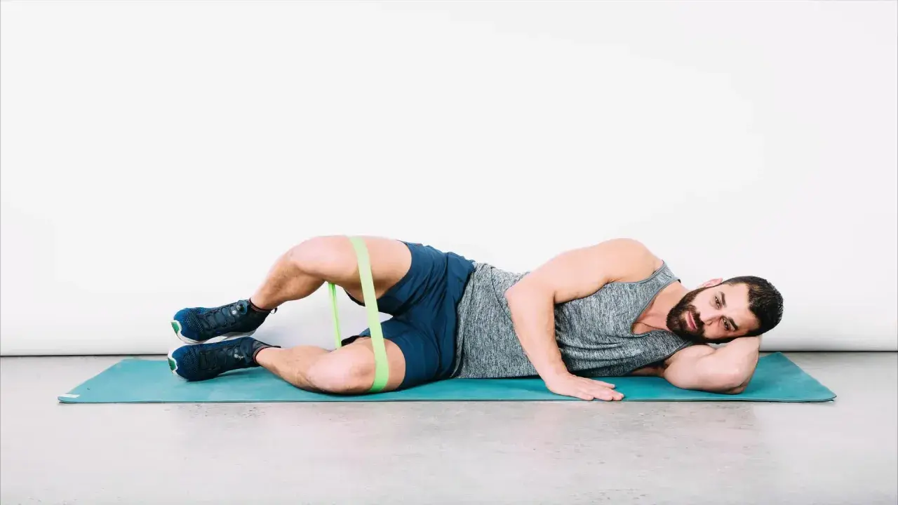 Uomo a terra con elastico intorno alle cosce per esercizi di bandelletta ileotibiale, soluzioni per rafforzare i glutei.