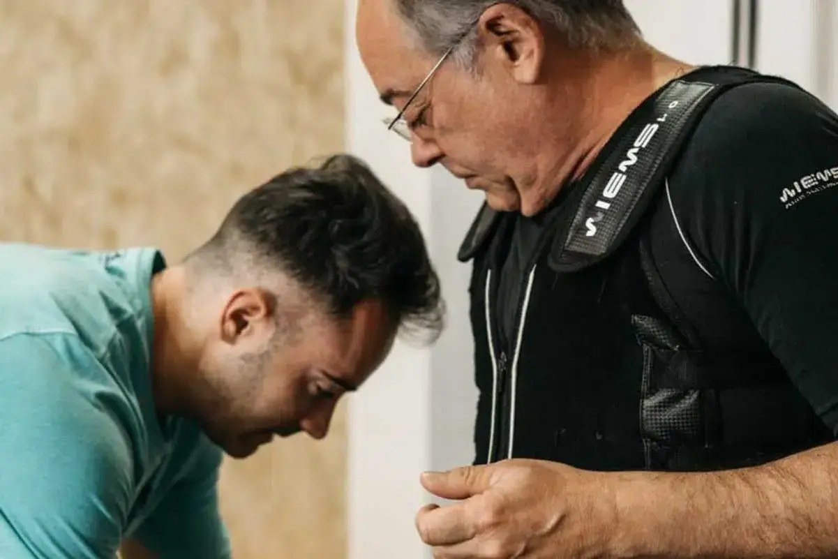 Uomo con giubbotto EMS, assistito da un trainer, per contrastare l'atrofia muscolare.