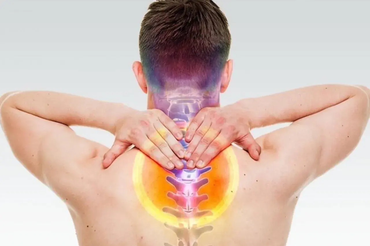 Uomo con mani sul collo e schiena, evidenziando dolore e possibili conseguenze di frattura vertebra cervicale.