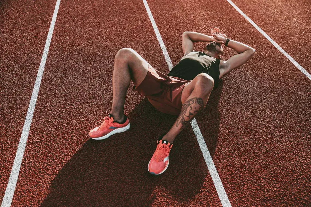 Atleta esausto sdraiato su una pista da corsa, mani sulla testa, forse uno dei sintomi del sovrallenamento.