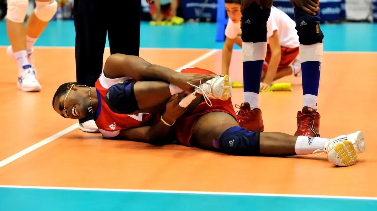 Giocatore di pallavolo a terra, con espressione sofferente, si tiene la caviglia. Un infortunio al volley caviglia durante la partita.