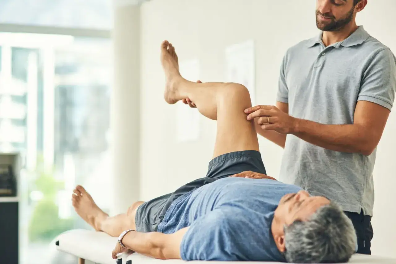 Fisioterapista valuta la gamba di un paziente, concentrandosi su un'area che potrebbe indicare atrofia muscolare, durante una sessione di riabilitazione.