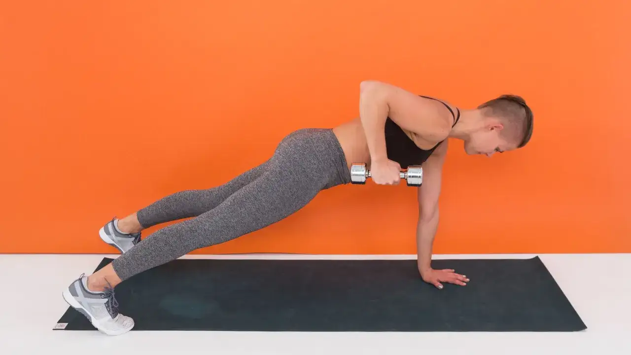 Donna in posizione plank esegue un rematore con manubrio, allenando la schiena e prevenendo la