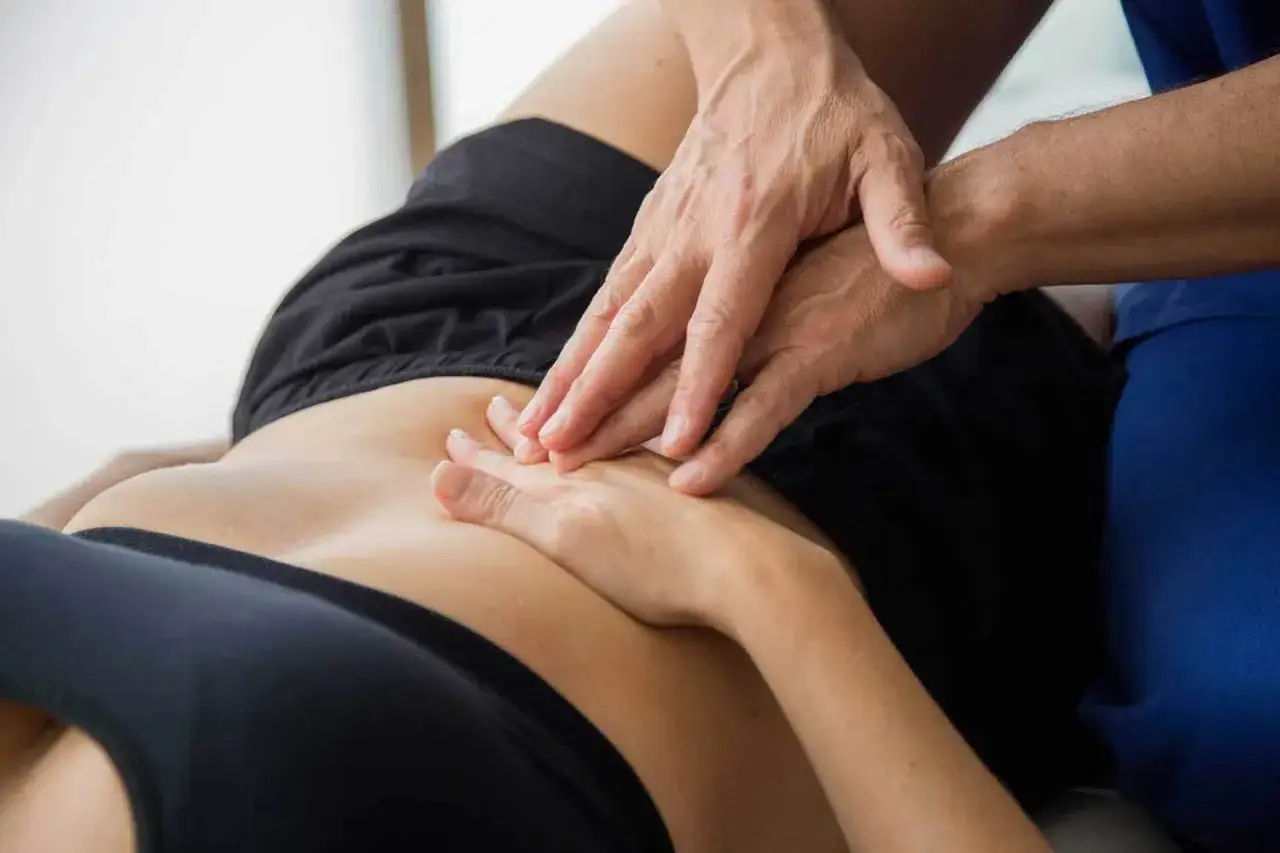 Mani di un fisioterapista che massaggiano l'addome di una paziente, aiutandola a superare il dolore legato al camminare con pubalgia.
