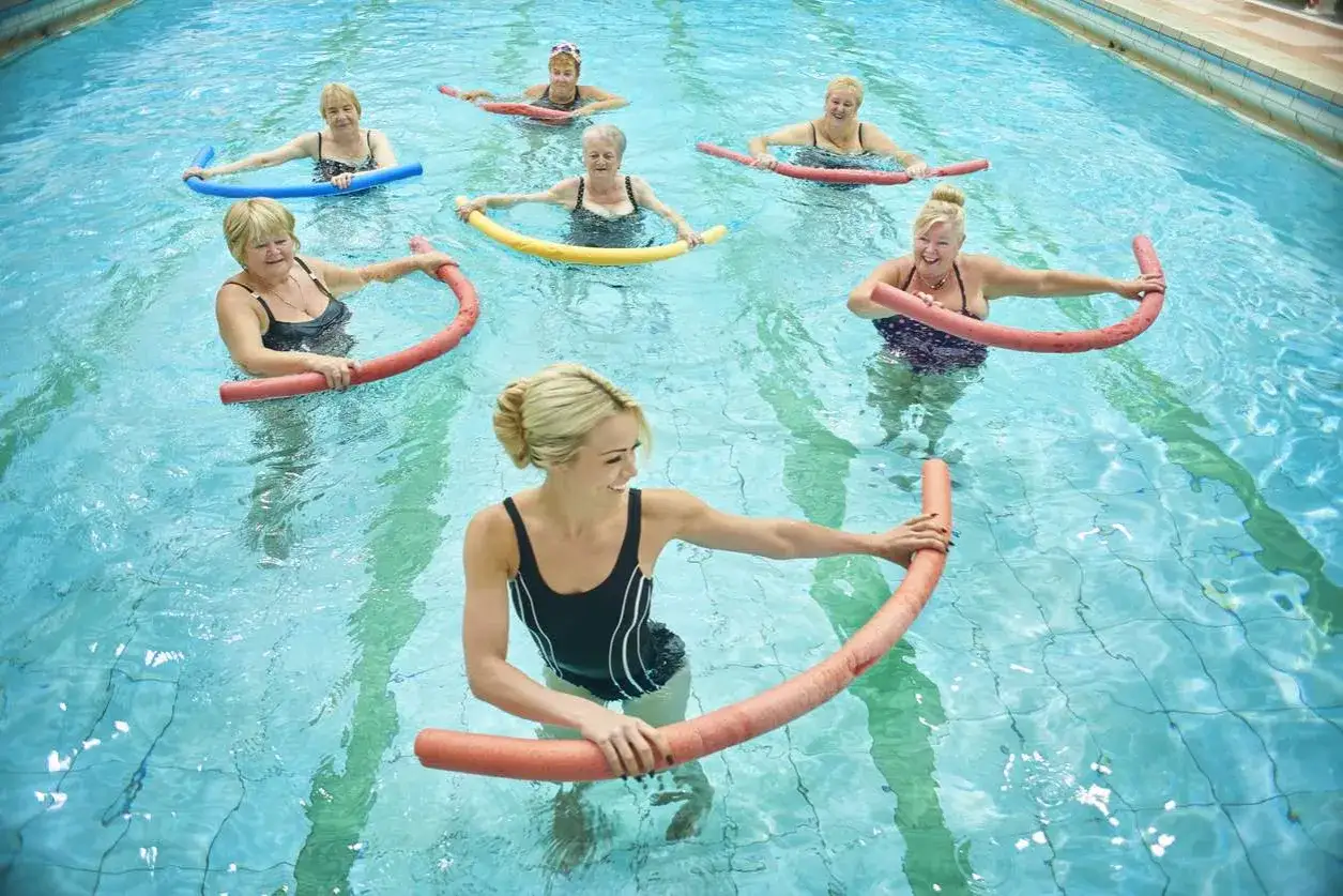 Donne anziane sorridono mentre svolgono esercizi in acqua per la schiena con galleggianti colorati.